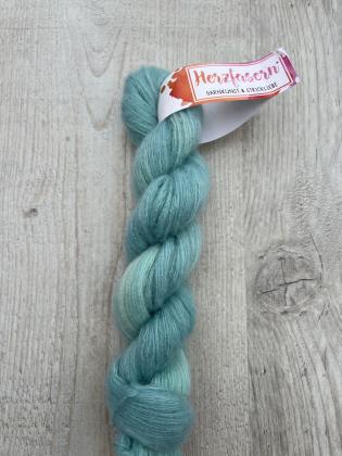 Abgebildet ist ein Strang Herzfasern No. 93 (Cashmere-Seiden-Lace) in einem changierenden Aquablau. Der Strang wirkt leicht, luftig und zeigt den charakteristischen feinen Glanz der Seidenmischung.